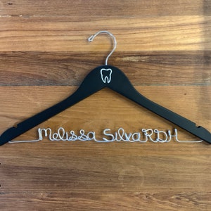May include: Black wooden hanger with a silver tooth design and the name "Melissa Silva RDH" written in silver wire.