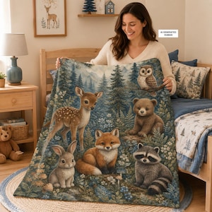 May include: A rectangular throw blanket featuring a detailed forest scene with a fawn, a fox, a rabbit, a raccoon, a bear cub, and an owl. The design includes pine trees, ferns, and small white flowers in shades of brown, green, and blue.