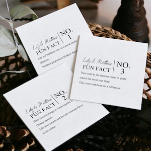 Può includere: Biglietti quadrati bianchi con testo nero, con i nomi "Lily & Matthius" e curiosità. I biglietti sono impilati, rivelando dettagli sull'incontro della coppia, i loro interessi e le esperienze condivise.