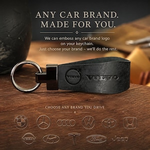 Peut inclure: Un porte-clés en cuir noir avec un anneau en métal et le logo Volvo embossé. Le texte indique : ANY CAR BRAND. MADE FOR YOU. We can emboss any car brand logo on your keychain. Just choose your brand – we’ll do the rest. CHOOSE ANY BRAND YOU DRIVE.
