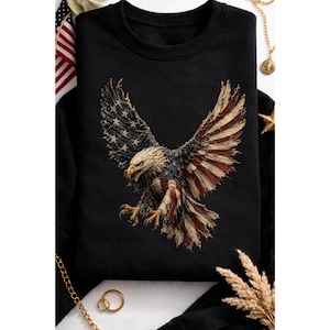 Op de afbeelding: Zwarte crewneck sweatshirt met een gedetailleerde afbeelding van een Amerikaanse Amerikaanse zeearend met wijd gespreide vleugels. De vleugels van de adelaar zijn ontworpen met de sterren en strepen van de Amerikaanse vlag. Het ontwerp is in tinten rood, wit, blauw en bruin.