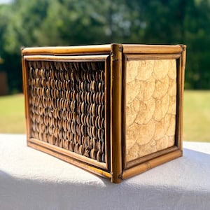 May include: A rectangular storage box featuring a bamboo frame. The front panel is constructed from dark brown woven seagrass in a tight grid pattern, while the side panel displays a light beige, circular shell-like mosaic tile inlay design.