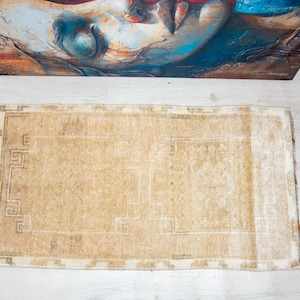 May include: A rectangular area rug featuring a light tan and beige color palette with a faded, intricate geometric border pattern. The rug has a low-pile texture and a worn, weathered appearance with subtle variations in the neutral tone throughout.