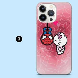 May include: A clear phone case with a pink spiderweb design. The case features a cartoon illustration of Spider-Man hanging upside down and Hello Kitty. Two pink hearts float above Hello Kitty. The number 3 is in a black circle.