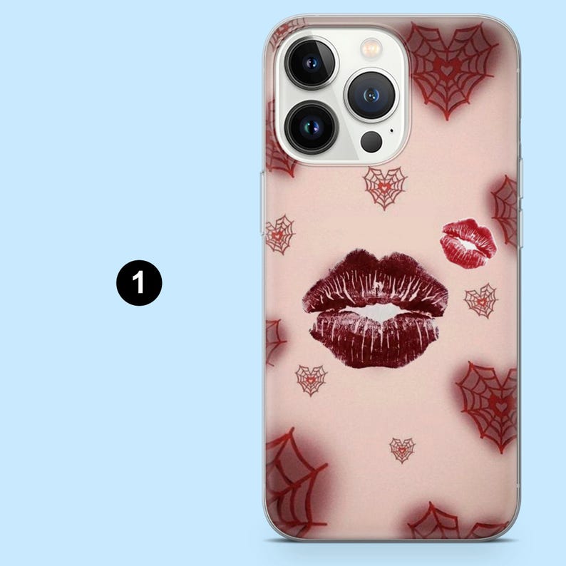 May include: A clear phone case with a pink background featuring a large, dark red lipstick kiss print and a smaller red lip print. Red spiderweb heart designs are scattered across the case.