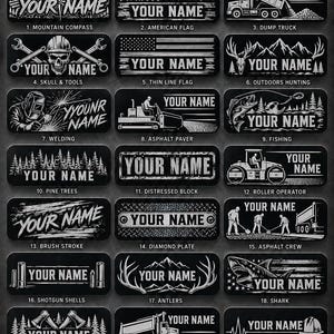 May include: A collection of twenty-one rectangular black and white hard hat nameplates featuring various engraved designs including a mountain compass, American flag, dump truck, skull, welding, fishing, pine trees, and shark with custom name text.