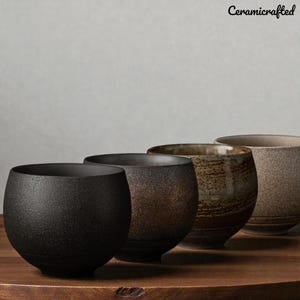 May include: Four ceramic bowls in a row, each with a unique texture and colour. The bowls range from black to brown and tan, with a textured finish. The bowls are on a wooden surface, with the text "Ceramicrafted" in the top right corner.