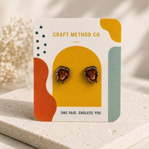 May include: A pair of stud earrings shaped like roasted chickens, displayed on a white card with the text CRAFT METHOD CO and ONE PAIR. ENDLESS YOU. The card features abstract shapes in mustard yellow, burnt orange, and sage green colors.