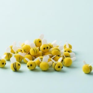 May include: A collection of small, yellow bee-shaped ornaments with black stripes and white wings. The ornaments are clustered together on a light blue background, creating a playful and whimsical scene. These decorative items are ideal for crafts or seasonal decor.