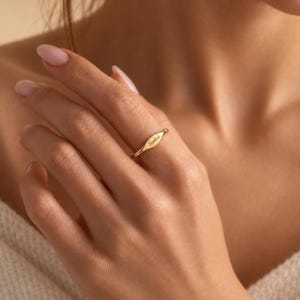 Puede incluir: Un anillo de tono dorado con una banda delgada y pulida que se ensancha en una barra horizontal central ligeramente curvada. La superficie de esta barra está grabada con el nombre Sophia en una fuente cursiva delicada y fluida, creando un aspecto refinado.