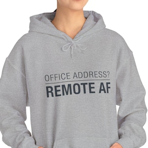 Könnte beinhalten: Ein hellgrauer Kapuzenpullover mit Kordelzug und Vordertasche. Der Text "OFFICE ADDRESS? REMOTE AF" ist in Schwarz auf der Vorderseite aufgedruckt. Der Hoodie ist aus einem weichen Material.