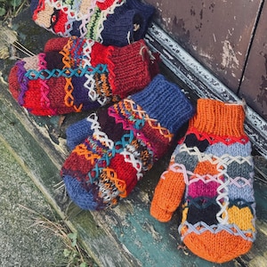 Puede incluir: Una colección de coloridas manoplas tejidas a mano. Las manoplas presentan un diseño de patchwork con varios colores, incluyendo azul, rojo, naranja y verde. Cada manopla tiene un patrón único con costuras decorativas.