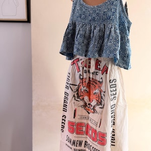Può includere: Un completo a due pezzi con un top blu fantasia e una gonna realizzata con un sacco di semi riutilizzato. La gonna presenta una grafica di tigre e il testo "TIGER BRAND SEEDS" e "SOMMEW BROSSEED CO".