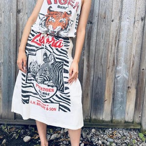 Peut inclure: Ensemble deux pièces confectionné à partir de sacs de pommes de terre recyclés. Le haut présente un motif de tigre et les mots "Tiger Brand". La jupe a un imprimé zébré et le mot "Zebra". L'ensemble est blanc avec des accents rouges et noirs.