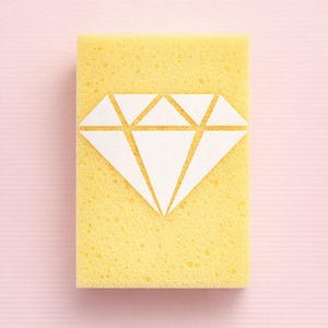 May include: A yellow rectangular sponge featuring a white diamond design. The sponge has a porous texture and is set against a light pink background. The diamond graphic is centered on the sponge.