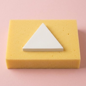 May include: A white triangle shape sits atop a yellow rectangular foam block. The background is a solid pink color. The image is a studio shot, likely for a product display or educational purpose.