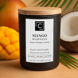 May include: A black candle with a wooden lid, labeled "MANGO MADNESS." The label lists mango, pineapple, and coconut scents. The candle is 8 oz / 226 g and made with soy wax. A mango and coconut are in the background.