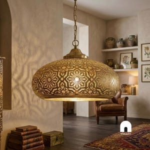 May include: A brass pendant light with a wide, dome-shaped shade featuring intricate, laser-cut geometric star patterns. The fixture is suspended by a matching brass chain and emits a warm, diffused light through the detailed metal cutouts.
