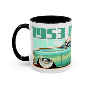 May include: A white ceramic mug with a black interior and handle, featuring a graphic of a teal vintage car and the text 1953 B. The car has white-wall tyres and chrome hubcaps, set against a white background with large teal lettering.