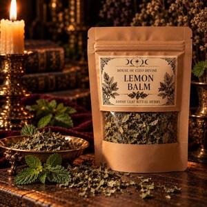 May include: A brown kraft paper pouch containing dried lemon balm, with a label reading House of Cleo Devine Lemon Balm Loose Leaf Ritual Herbs. The pouch has a clear window showing the green dried herbs inside.