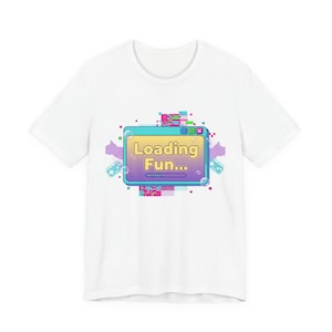 May include: White t-shirt featuring a colorful graphic of a computer window with the text "Loading Fun...". The design includes pixelated elements, arrows, and a retro gaming aesthetic. A fun and playful design.