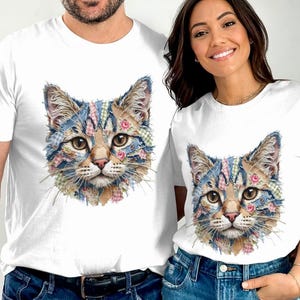 以下が含まれることがあります： 詳細な猫の顔のデザインが施された白いTシャツ。猫の毛皮は、青、ピンク、緑の生地のパッチワーク模様で、花のアクセントが付いています。猫は大きく、表情豊かな目をしています。シャツは2人で着用しています。