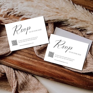 Op de afbeelding: Twee witte RSVP-kaarten met elegant zwart schrift en een QR-code worden weergegeven op een houten dienblad. De kaarten bevatten de tekst "BY 1ST JUNE 202X" en website-informatie. De achtergrond heeft beige stof en gedroogde planten.