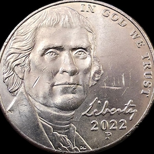 May include: A silver-colored United States five-cent coin featuring a profile portrait of Thomas Jefferson. The text IN GOD WE TRUST is arched along the right side, with the word Liberty and the year 2022 followed by a P mint mark below it.