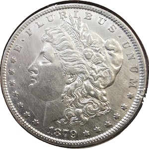 May include: A silver Morgan dollar coin dated 1879, featuring a profile of Lady Liberty facing left, wearing a cap with the word LIBERTY, surrounded by the text E PLURIBUS UNUM, thirteen stars along the rim, and a beaded border edge.