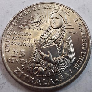 May include: A silver-colored United States 25 cents coin featuring a portrait of Zitkala-Sa holding a book. The text reads UNITED STATES OF AMERICA, E PLURIBUS UNUM, AUTHOR, ACTIVIST, COMPOSER, 25 CENTS, and ZITKALA-SA, with a bird and sun rays.