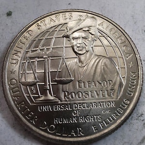 May include: A silver-colored United States quarter dollar coin featuring a portrait of Eleanor Roosevelt, a scale of justice, and a globe background. The text reads UNITED STATES OF AMERICA, ELEANOR ROOSEVELT, UNIVERSAL DECLARATION OF HUMAN RIGHTS, and E PLURIBUS UNUM.