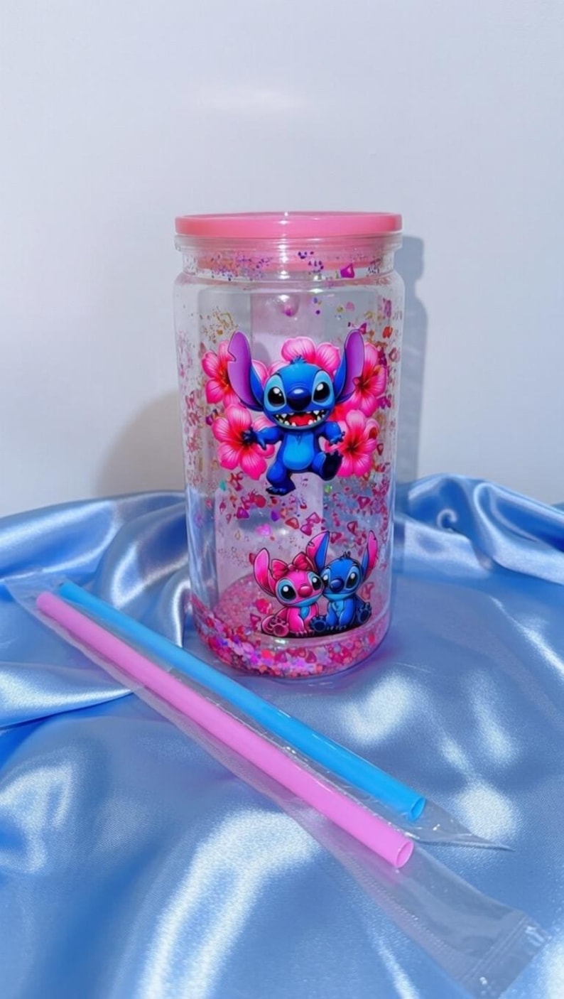 K&ouml;nnte beinhalten: Ein klarer, zylindrischer Becher mit rosa Deckel, mit einer blauen Cartoonfigur mit rosa Blumen. Der Becher ist mit rosa Glitzer gef&uuml;llt und enth&auml;lt rosa und blaue Strohhalme.