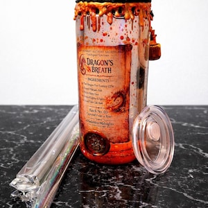 May include: A clear glass jar labeled "Dragon's Breath" with a black lid and orange wax drips. The jar has a label with text and a seal. A clear lid and a package of straws are next to the jar. The jar is on a black surface.
