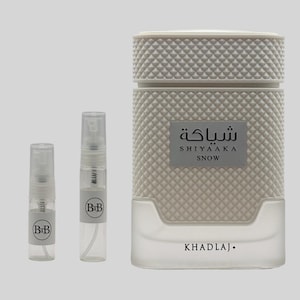 May include: A white perfume bottle with a textured diamond pattern, accompanied by two small sample spray bottles. The main bottle has a rectangular label with Arabic text and the word "SNOW". The brand name "KHADLAJ" is printed at the bottom.