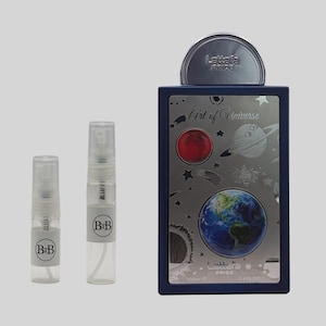 May include: A perfume set featuring a dark blue rectangular bottle with a silver design of planets and the Earth, labeled "Art of Universe." Two small spray bottles with "BiB" labels are also included. The set is against a light gray background.
