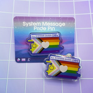 May include: Two clear acrylic pins with a rainbow pride flag and a heart. The text on the pins reads "All Systems Queer".