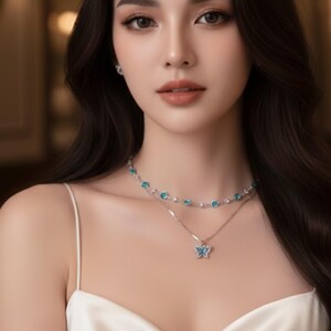 Peut inclure: Une femme porte un haut en satin blanc et deux colliers délicats. Le collier supérieur présente de petites pierres bleues, tandis que le collier inférieur a un pendentif papillon avec des accents bleus. La femme a de longs cheveux foncés et regarde la caméra.
