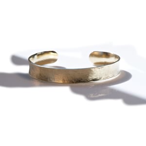 May include: A gold-toned metal cuff bracelet with a hammered finish.