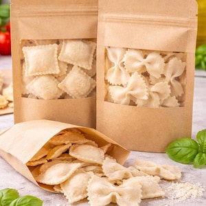 May include: Three brown paper bags with clear windows displaying various pasta shapes: ravioli, bow tie, and a mix. Some pasta spills onto a light grey surface, with basil leaves and a bottle of oil in the background.