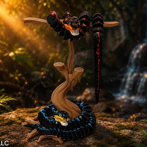 Könnte beinhalten: Detaillierte Skulptur einer Schlange in einer Dschungelumgebung. Die Schlange ist schwarz mit roten und orangen Akzenten, am Fuß eines Holzständers aufgerollt und auf einem Ast platziert. Ein Wasserfall und üppiges Laubwerk befinden sich im Hintergrund.