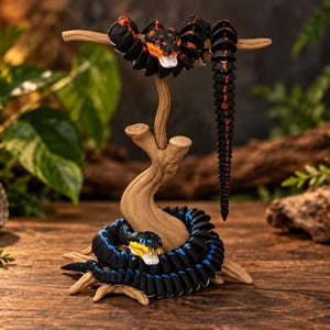 May include: Two articulated snake figures made of black plastic with segmented bodies. One snake features orange accents and is coiled around the top of a tan, tree-like stand. The second snake has blue accents and is coiled around the base of the stand.