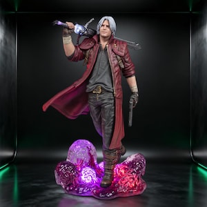 May include: A detailed collectible figurine of a silver-haired character wearing a long red coat, dark shirt, and pants. The figure holds a large sword across their shoulders and a handgun in their left hand, standing on a glowing purple base.