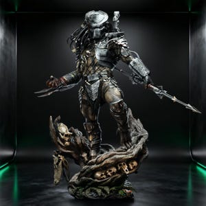 May include: A detailed statue of the Predator, a science fiction character, standing on a tree trunk base adorned with skulls. The figure is clad in metallic armour and carries bladed weapons. The statue has a silver helmet and dreadlocks.