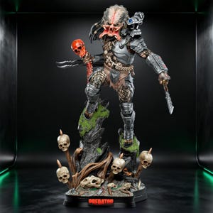 Peut inclure: Figurine détaillée de Predator, debout sur une base rocheuse avec des crânes et le mot "PREDATOR". La figurine est vêtue d'une armure métallique, tenant un bâton de crâne et une lame. Le visage du Predator est rouge et ses dreadlocks sont visibles.
