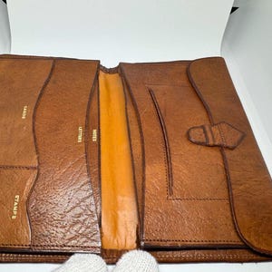 Op de afbeelding: Open bruin lederen organizer met vakken met de labels "CARDS", "STAMPS", "LETTERS" en "NOTES". De organizer heeft een flap met een gespsluiting. De binnenkant is een lichtere bruintint.