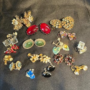 May include: A collection of vintage earrings in various styles and colors. The earrings include clip-ons and pierced styles, with gemstones, rhinestones, and floral designs. Colors include red, green, blue, gold, and clear.