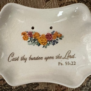 May include: Off-white ceramic soap dish with a scalloped edge. The dish features a floral design with yellow, pink, and orange roses. The text "Cast thy burden upon the Lord. Ps. 55:22" is printed below the flowers.