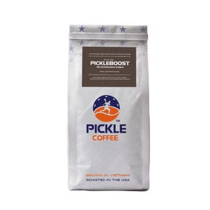May include: A white bag of Pickle Coffee, with the text "PICKLEBOOST" and "PICKLE COFFEE" in a dark brown and orange design. The bag also includes the text "GROWN IN VIETNAM" and "ROASTED IN THE USA".