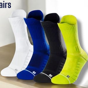 Könnte beinhalten: Vier Paar Sportsocken in Weiß, Blau, Schwarz und Neongrün. Jede Socke hat ein geripptes Design und einen weißen Akzent an Zehen und Bündchen. Der Text "4 Pairs" befindet sich in der oberen linken Ecke.