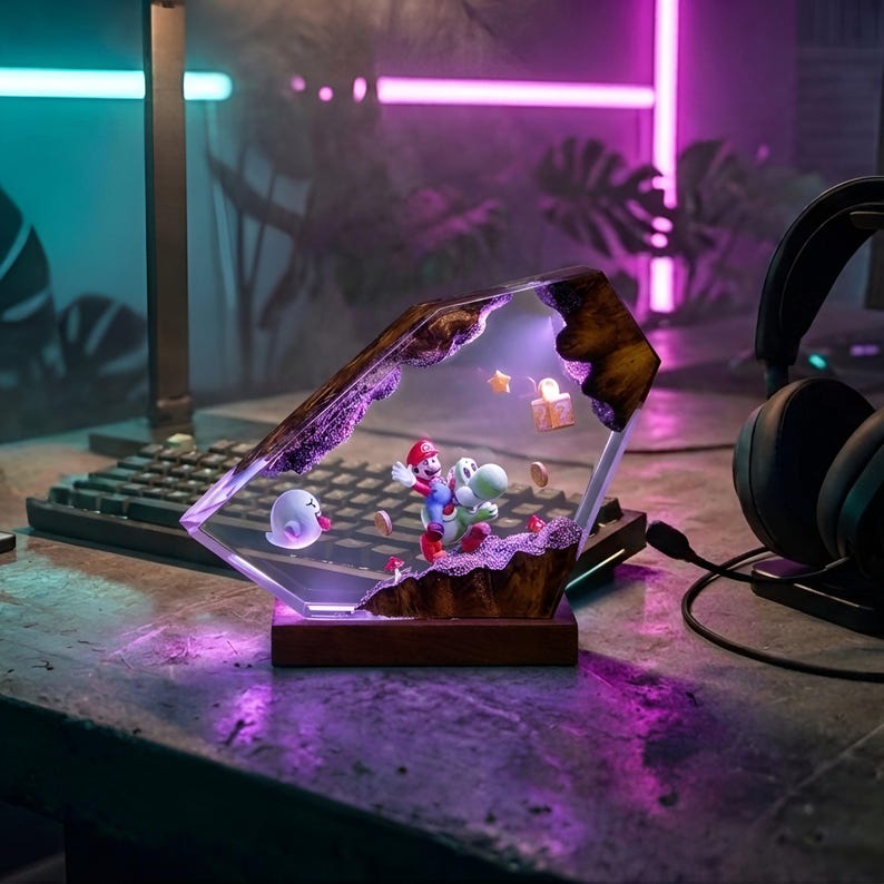 K&ouml;nnte beinhalten: Dekorative Lampe mit einer Szene mit Mario und Yoshi, einem Geist, Sternen und M&uuml;nzen. Die Lampe ist in einer klaren, abgewinkelten Struktur mit Holzsockel eingeschlossen. Im Hintergrund befinden sich eine Tastatur und Kopfh&ouml;rer.